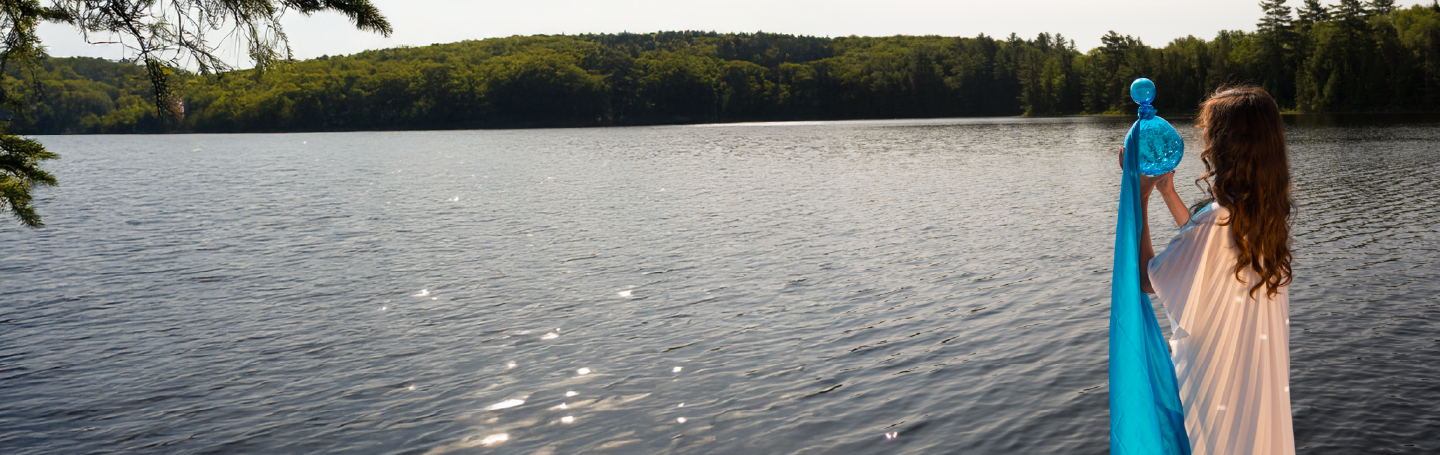 Woman holding a blue towel by a lake with trees in the background